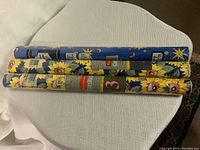 Three new rolls of Mactac adhesive vinyl with different prints laid on a white surface, unopened and unused.