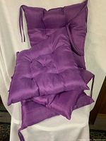Four stacked purple tufted chair cushions with corner ties shown on a white background.