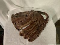 Side view of the brown leather baseball glove, showing the fingers and opening with elastic adjustment strap.