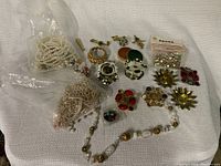 Photo showing mixed crafting beads, vintage-style brooches in floral and geometric styles, faux pearl strands, and various metal jewelry components.