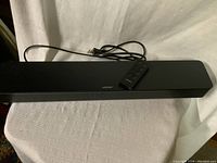 Front view of the black Bose sound bar with remote placed on top, showing Bose logo and power cord.