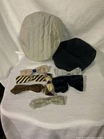 Front view of white quilted cap, black hat and seven varying bow ties laid out on fabric