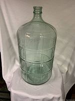 Clear glass carboy with embossed rectangular panels, narrow neck, and slight green tint.