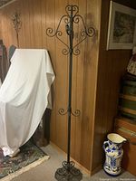 Photo showing the tall cast iron coat rack against a wood-paneled wall with various surrounding furniture and decors