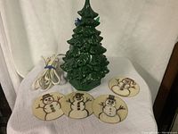 Full view of green glazed ceramic Christmas tree lamp with electrical cord and four round handmade snowman coasters in front