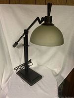 Full view of the adjustable black desk lamp with frosted dome shade and rectangular base, showing arm angle and base design.