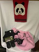 Photo showing all items: 2 black Mutt Tracker dog shoes, pink dog harness, pink dog coat sweater, red carry bag with panda face design.