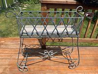 Metal garden plant stand standing upright showing diamond lattice sides and curled leg details.