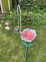Photo showing handmade Christmas flowers, watering can, flower holders, candle holders, and garden trellis placed on grass outside near garden foliage.