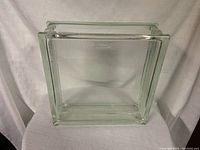 Clear square glass block with smooth edges and textured sides, placed on a cloth background.