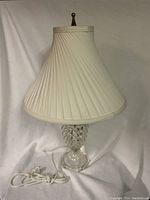 Clear photo of a glass lamp with a pleated white fabric shade on a white backdrop.