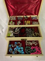 Top view of jewelry box showing multiple compartments filled with assorted costume jewelry including pins, bracelets, and necklaces