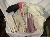 Nine pairs of assorted ladies gloves in various colors and materials laid out on fabric background.
