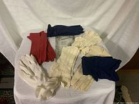 Seven pairs of ladies gloves displayed on white cloth background showing variety of colors and styles.