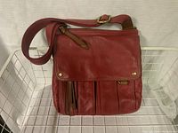 Front view of the red leather Fossil crossbody purse showing flap with two metal studs, front zipper pocket with leather pull, vertical stitched pocket details, and adjustable strap.