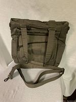 Front view of the olive green LUG tote bag showing multiple zippered pockets and handles, with additional shoulder strap placed in front.