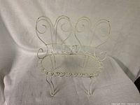 White metal doll chair with heart-shaped back and mesh seat shown on a white fabric background