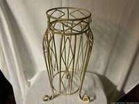 Metal plant stand photographed against a white curtain backdrop, showing the full stand with geometric and scroll details.