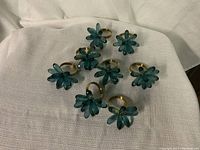Eight glass flower napkin rings with gold-colored bands arranged on a white cloth.