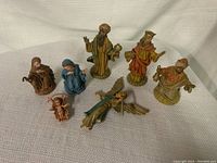 View of all 7 painted nativity figurines arranged upright on a fabric surface.
