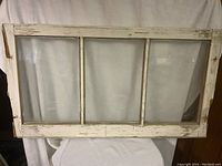 Photo of old wooden window frame with four glass panes and chipped white paint, showing signs of age and wear.