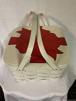 Photo of top of white wicker basket showing large red bow design and dual fabric straps crossing over lid