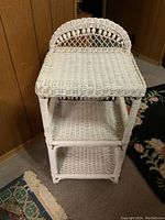 White wicker shelf with three shelves and decorative woven backrest, approx 32 inches tall.