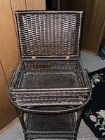 Wicker stand open showing inside storage compartment with hinged lid and woven wicker construction.