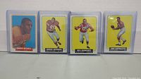 Four 1964 Topps NFL football cards featuring Charlie Mitchell, Junious Buchanan, Nick Buoniconti, and Gino Cappelletti displayed in protective sleeves.