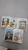 Stacked baseball card piles showing clear fronts with player photos and team names from 1977 Topps series including Blue Jays, Twins, White Sox, Mets.