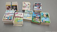 Multiple stacks of vintage baseball cards from various brands and teams on grey surface.