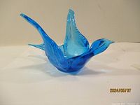 Blue glass art bird figurine with wings spread viewed from front.