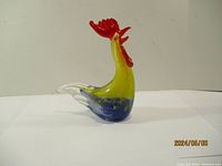 Front and side views of the colorful art glass rooster figurine, showing its shape, color gradient, and clear glass tail.