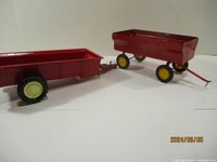 Pair of red metal farm trailers, one 13 inches long and one 10 inches long, showing their general shape and wheels.