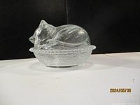 Glass cat figurine displayed on a dark background showing side angle of curled cat sleeping on basket base