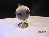 Glass globe desk ornament with etched continents and grid lines, sitting on a silver-tone metal stand with a round base, shown from an angle