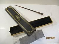 Full view of the Ron Weasley wand alongside its black and gold-trimmed box and gray pouch.