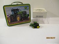 Photo showing John Deere lunchbox with tractor image, Hallmark box, clear plastic insert, and tractor ornament.