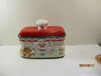 Full view of the large ceramic bread bin with red lid and white knob, showing its approximate size and decoration.