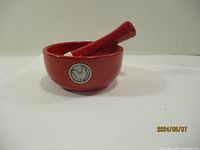 Front view of red ceramic mortar and pestle showing rooster emblem on mortar.