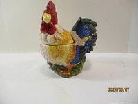 Left side view of ceramic rooster cookie jar with vibrant coloring and textured detail.