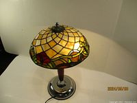 Full view of the Tiffany style stained glass lamp showing amber geometric pattern and floral decorative accents.
