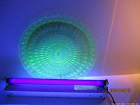 Uranium glass platter glowing bright green under UV light, showing geometric, faceted pattern and scalloped edge.