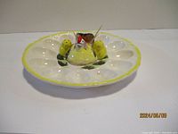 Side angled photo of the white ceramic deviled egg plate with 12 wells and a central decorative chicken salt and pepper shaker set with toothpick holder.