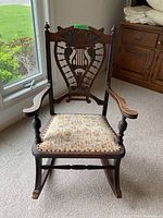 Full front view of carved wood rocking chair with needlepoint seat