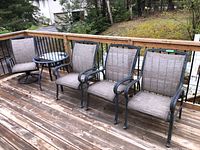 Full view of four outdoor patio chairs arranged on deck with one small round side table between them.