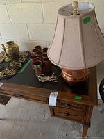 Overall view of the copper items including the lamp, mugs, candlesticks, and decorative containers on a wooden table.
