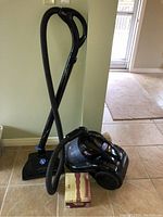 Side view of black Fantom vacuum cleaner with hose and upright floor attachment, showing overall unit.