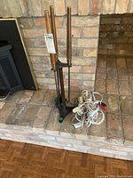 Fireplace tool set with wooden handles on a black metal stand next to white extension cords placed on brick hearth.
