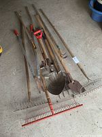 Photo showing a set of garden tools including rakes, shovels, hoes, and clippers laid out on concrete floor
